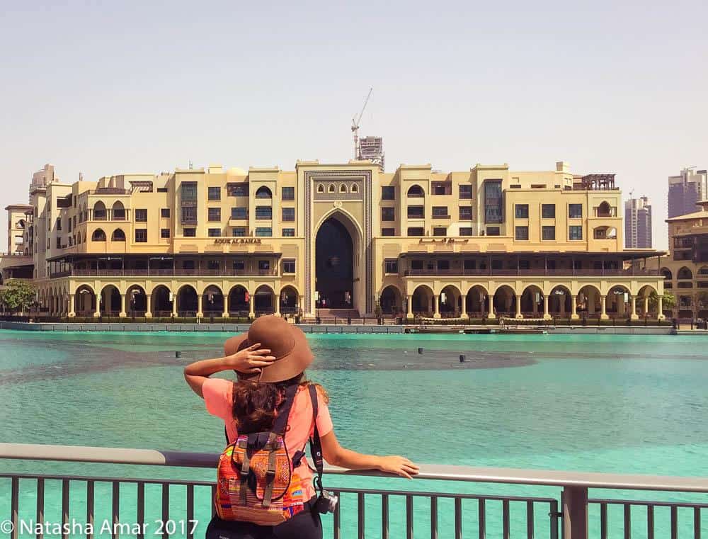 A girl in a tshirt and jeans, holds one hand to a hat and gazes at the Palace Downtown Hotel in Dubai