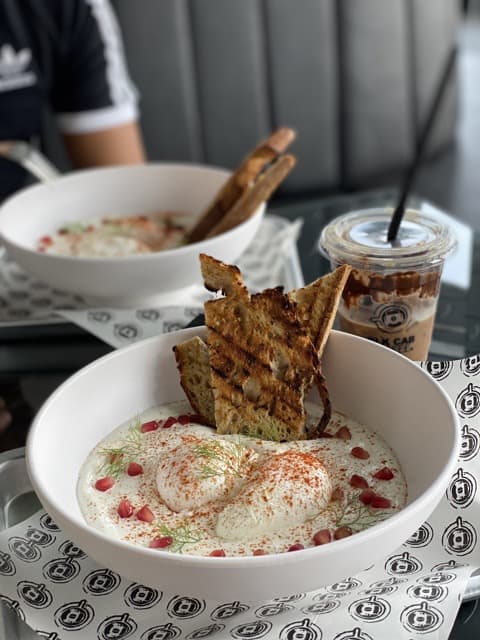 Turkish eggs - poached eggs swimming in yogurt, topped with dill and pomegranate seeds, also dipped are slices of toasted bread