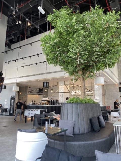 Cafe interior with gray couch seating around a fake tree in the center