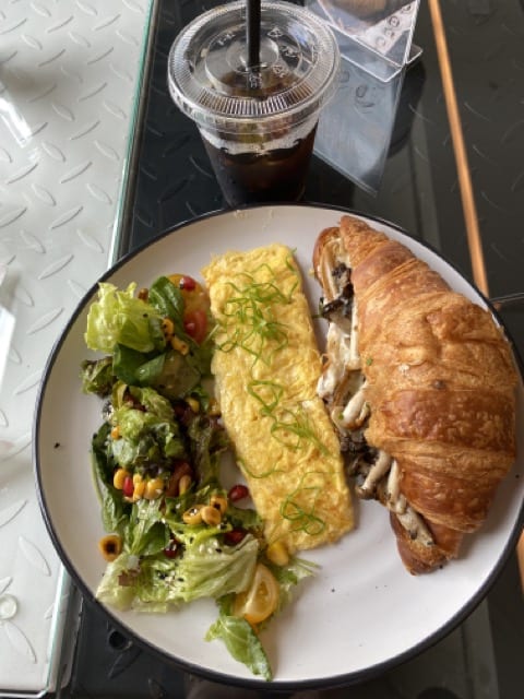 Mushroom stuffed croissant, an omelet, and a side salad of leaves and corn on a plate