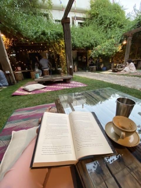 An open book on a low glass table in a tree filled garden cafe 