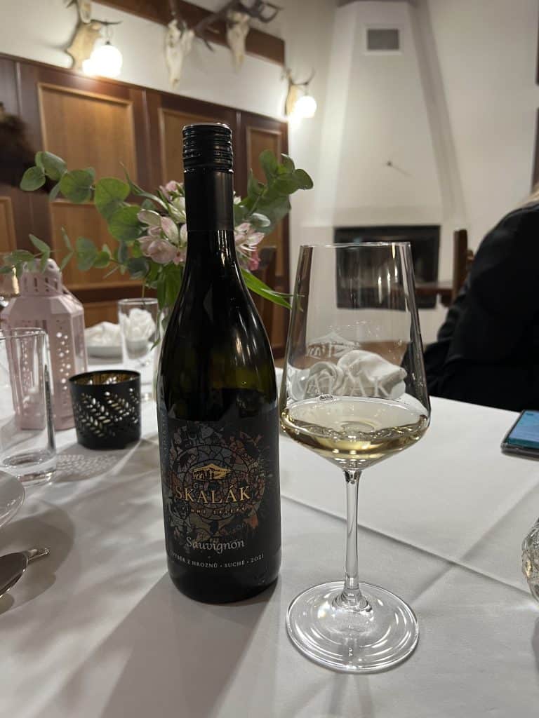 A glass of white wine next to a bottle that reads Skalak Sauvignon.