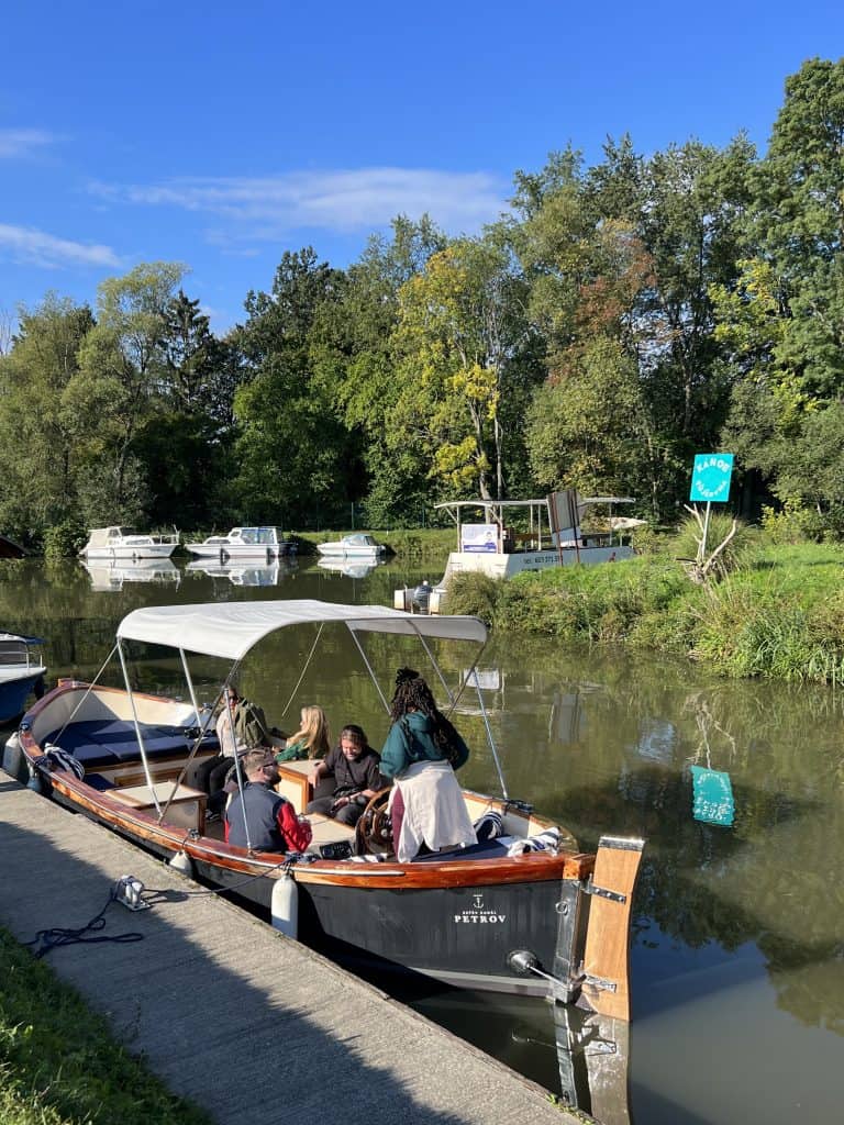 A boat with a white shade on a canal surrounded by trees. There are people in the boat.