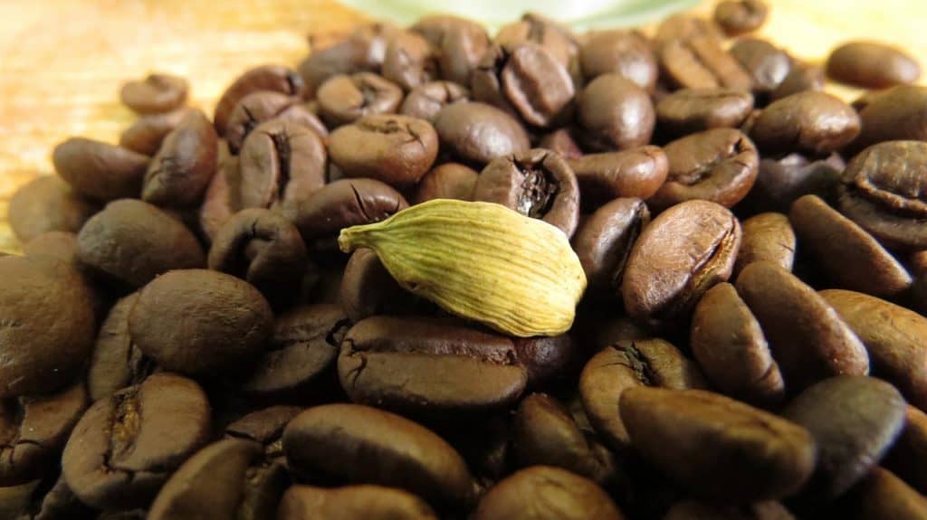 a heap of Coffee beans with a cardamom pod on top 