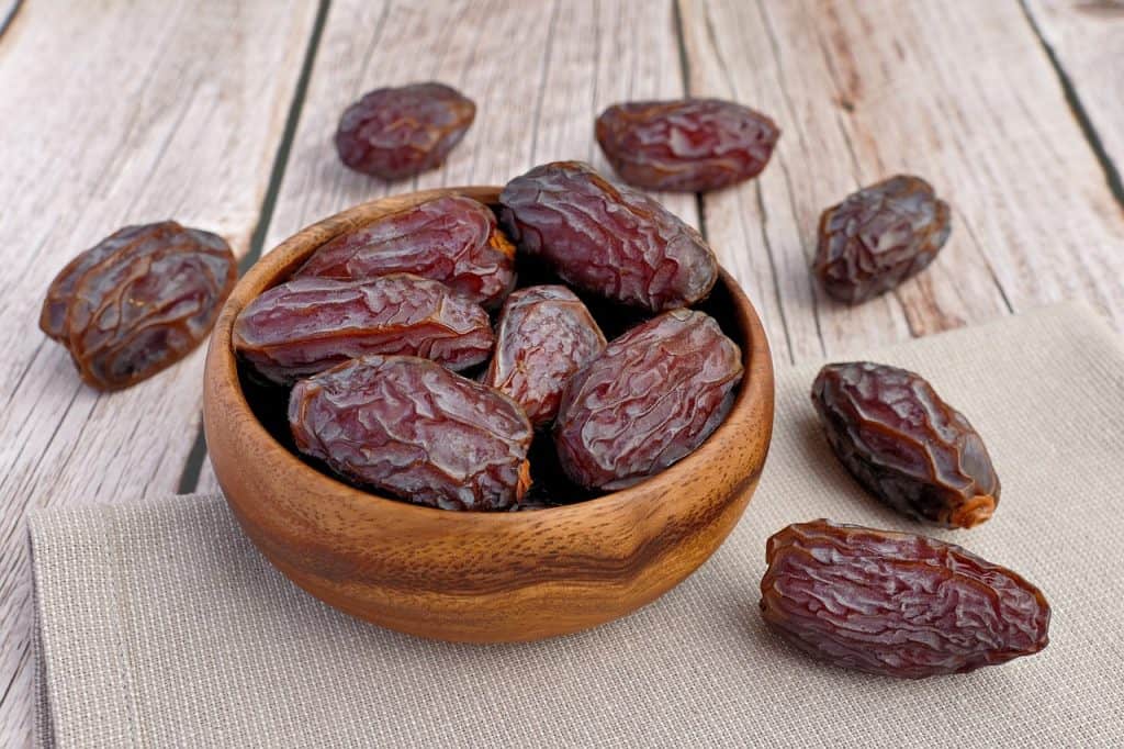 Dark brown dried dates in a round bowl on a wooden tabletop