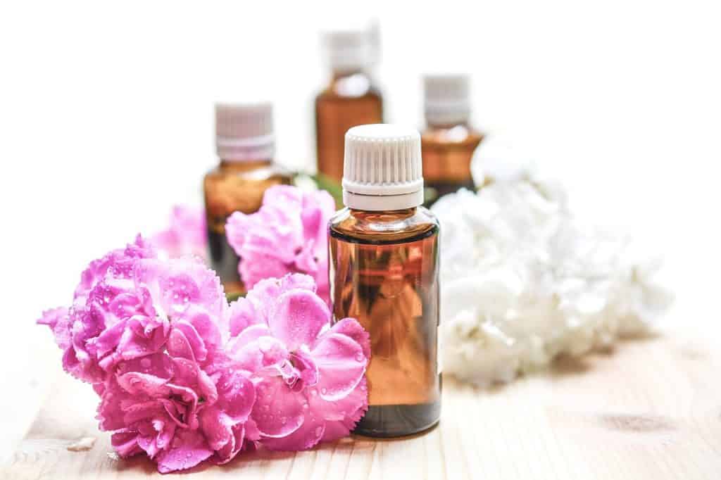 Four small bottles of essential oils placed among pink and white flowers