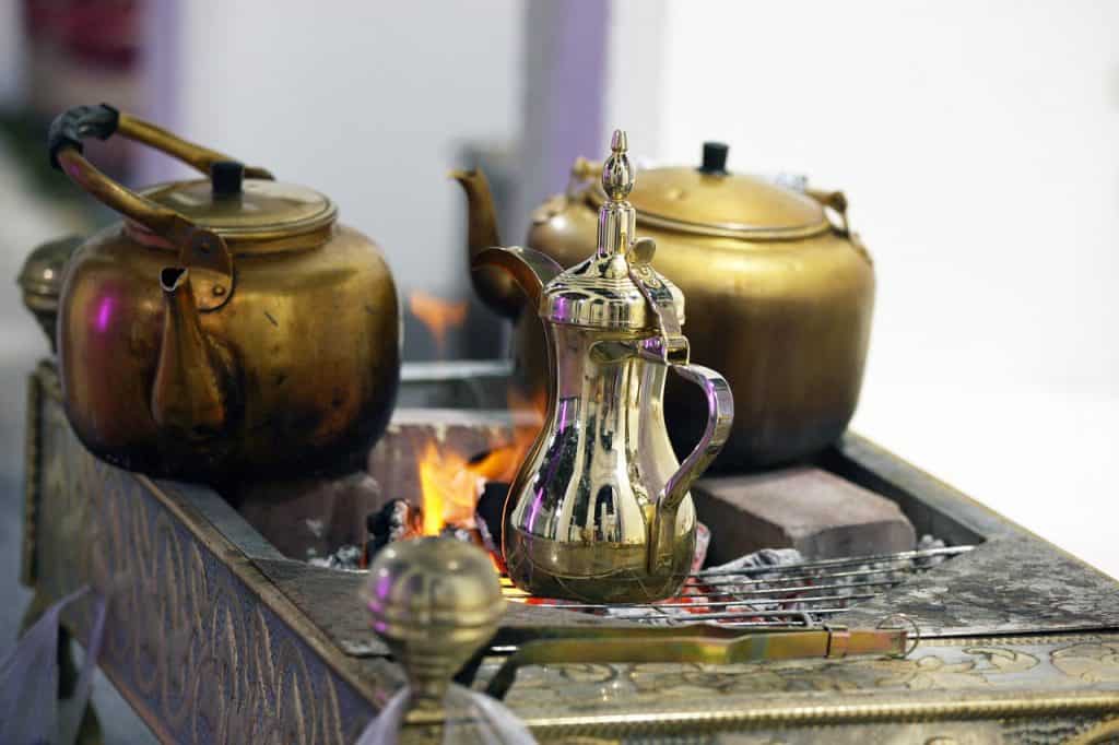 A coffee pot on a fire, next to it are other brass coffee pots