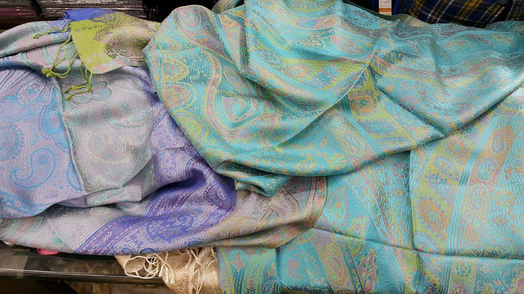 A few pashmina shawls kept for display one over the other. The one on top if turquoise and a bit of a lavender pashmina peeks from underneath. 